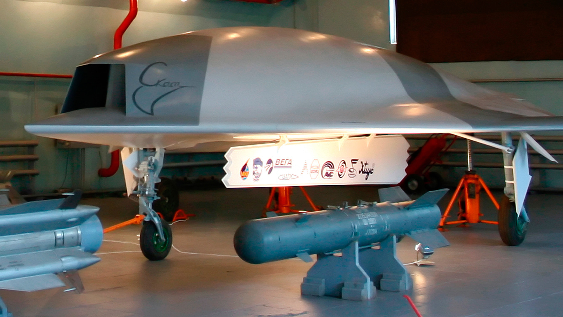 Model brezpilotnika Skat v naravni velikosti (zadaj) in bombe KAB-500 (spredaj) v hangarju ruskega letalskega proizvajalca MiG na 8. letalskem mitingu MAKS-2007 v kraju Žukovski.