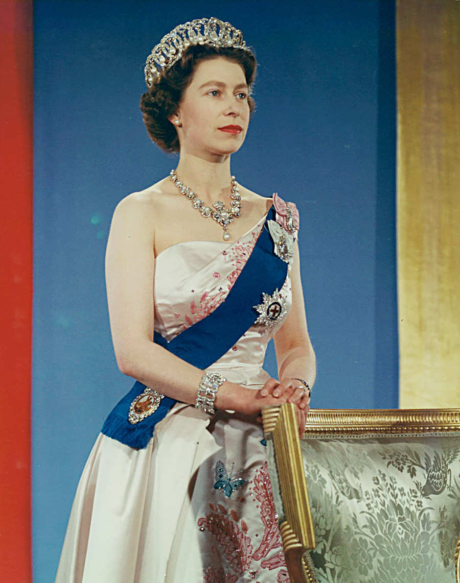 Queen Elizabeth II wearing crown, blue sash and pink gown.