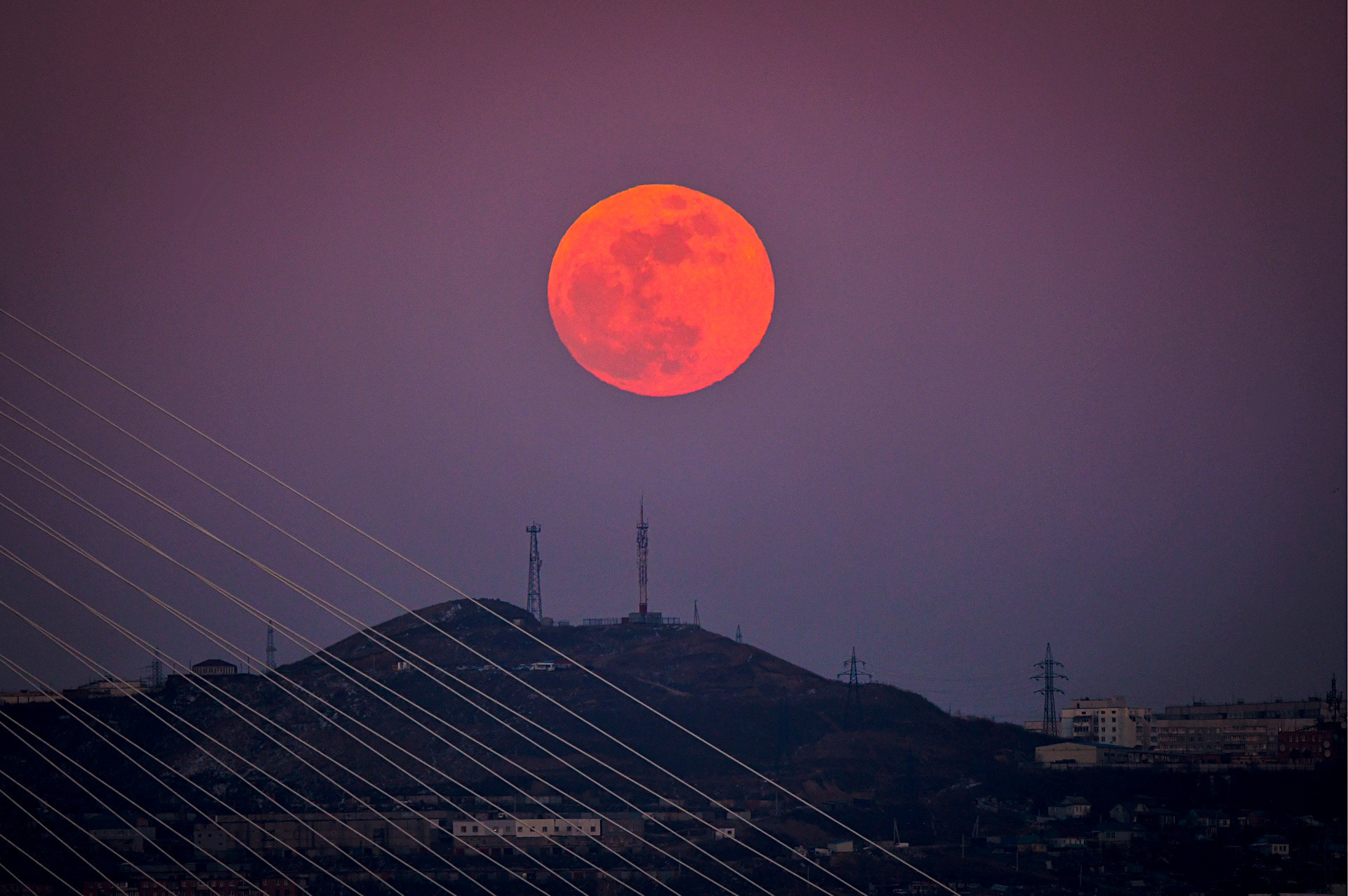 Vladivostok, Rusia: Bulan purnama merah terbit di atas bukit kota Vladivostok di Timur Jauh Rusia, sementara bulan biru, bulan super, dan gerhana bulan total terjadi di saat yang sama.