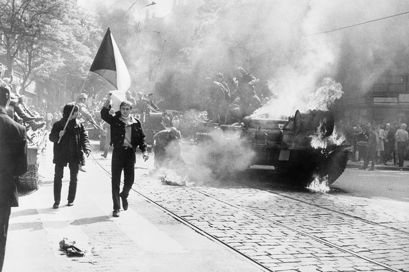 Invasi Soviet ke Cekoslowakia. Warga Cekoslowakia membawa bendera nasional melewati tank yang terbakar di Praha, 1968.