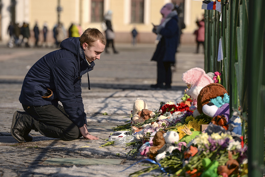 A man kneels near a spontaneous memorial on Dvortsovaya Square in St. Petersburg.