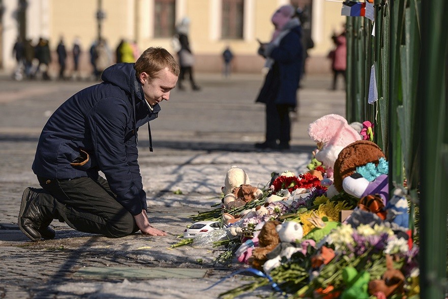 Moški v počepu poleg spontano nastalega mesta za poklon žrtvam, trg Dvorcovaja, Sankt Peterburg.