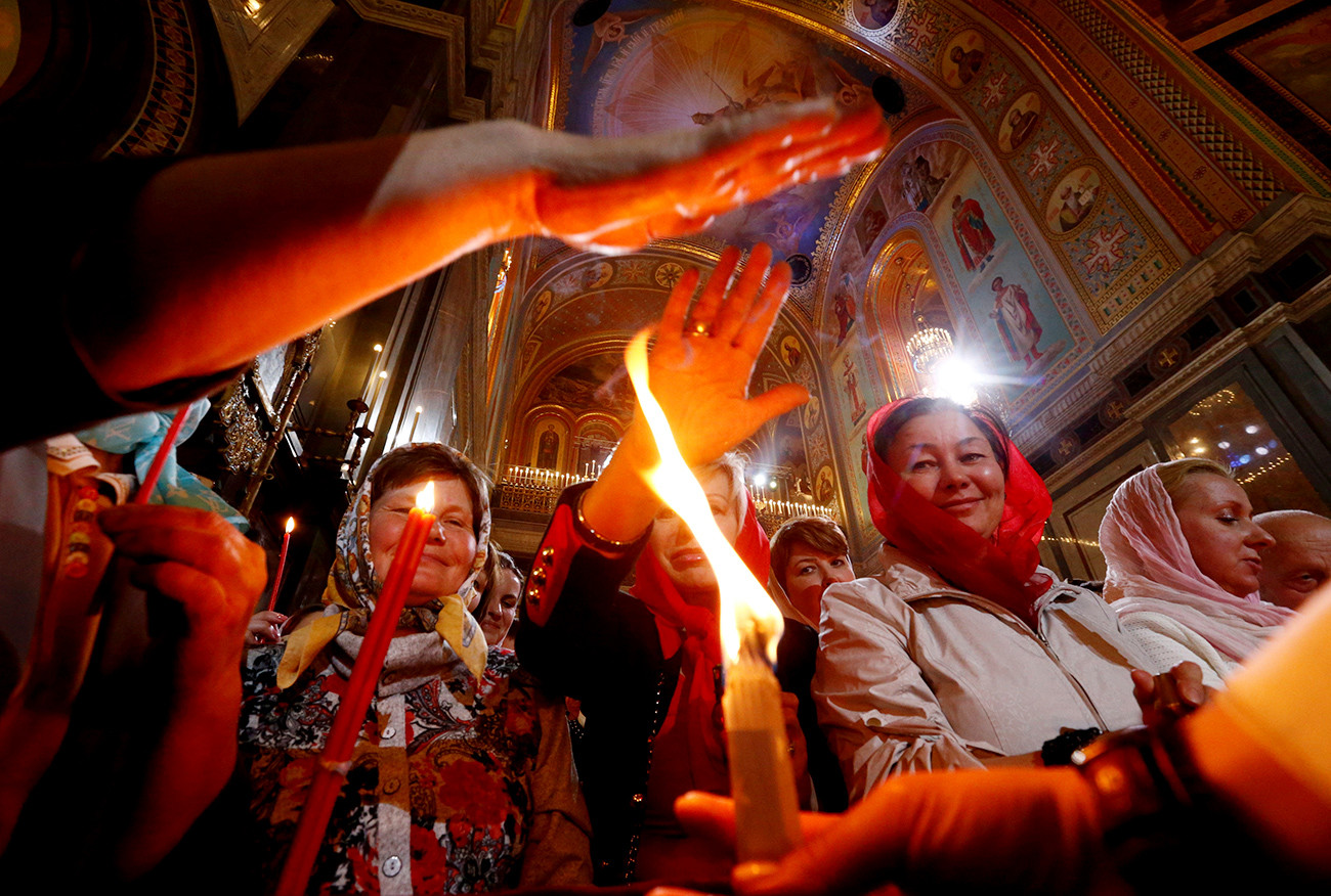 Creyentes se acercan a tocar las velas del Fuego Sagrado durante una misa ortodoxa de Pascua en la Catedral de Cristo Salvador de Moscú.