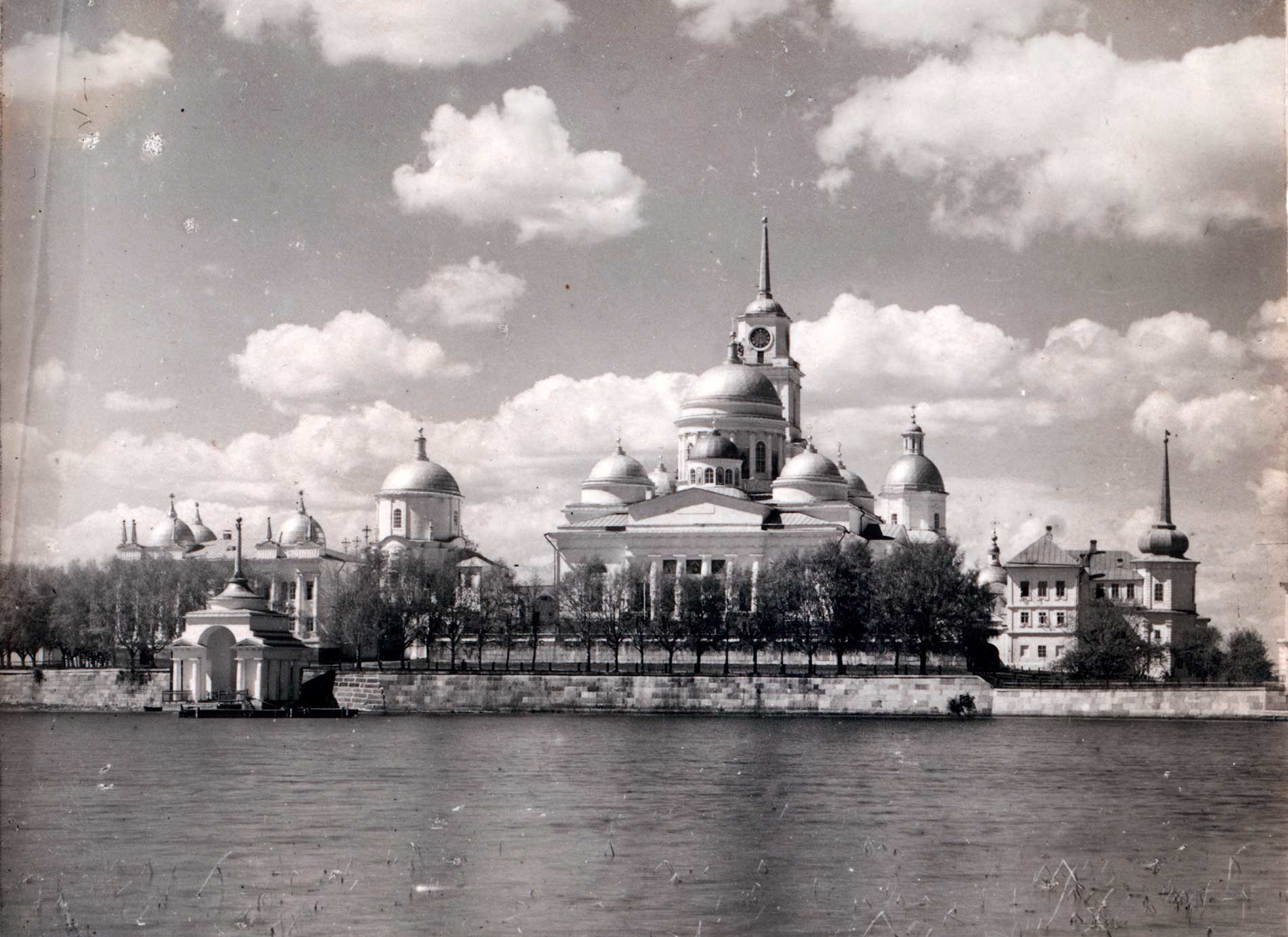 Nilova Pustyn, east view from small island. From left: Archbishop's Landing, Archbishop's Chambers, Church of St. Nilus Stolobensky over East Gate, Epiphany Cathedral&bell tower, Church of SS. Peter&Paul over West Gate, Church of All Saints, Refectory. Summer 1910.