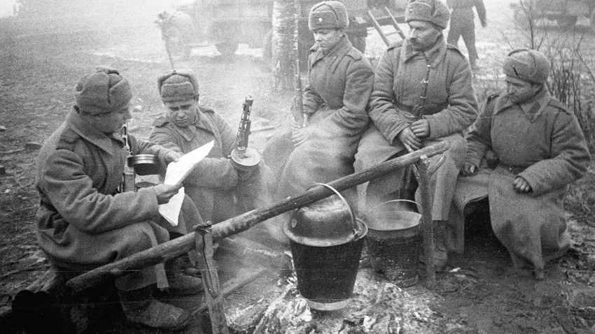 Sovjetski vojaki kuhajo obrok, berejo časopis in se grejejo ob ognju. 