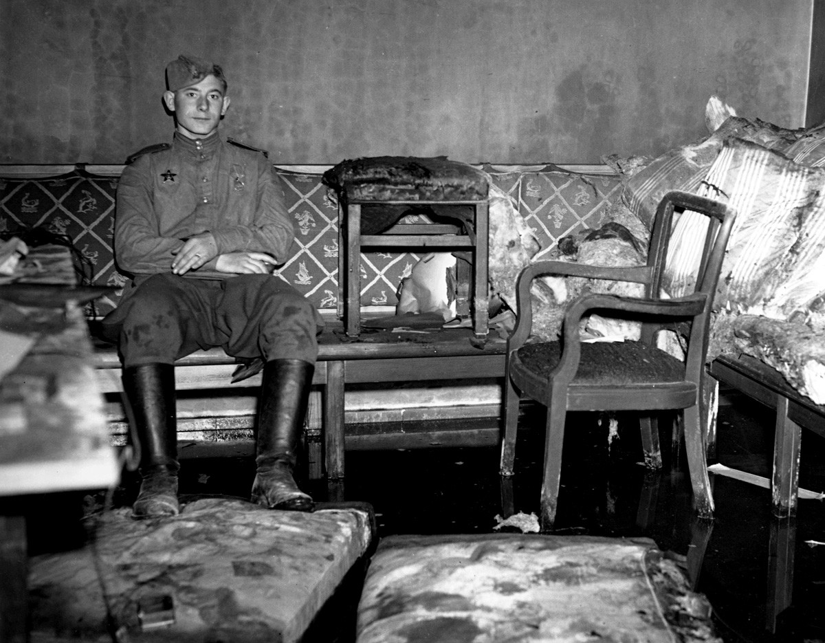 Ein sowjetischer Soldat sitzt auf dem Sofa, auf dem Adolf Hitler Selbstmord begangen haben soll.