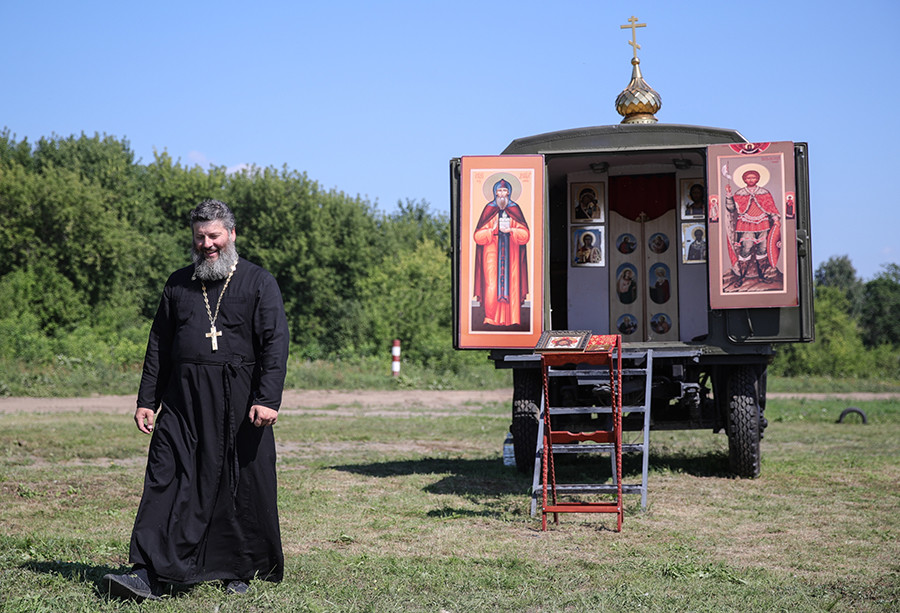 Padre ortodoxo diante de capela móvel.