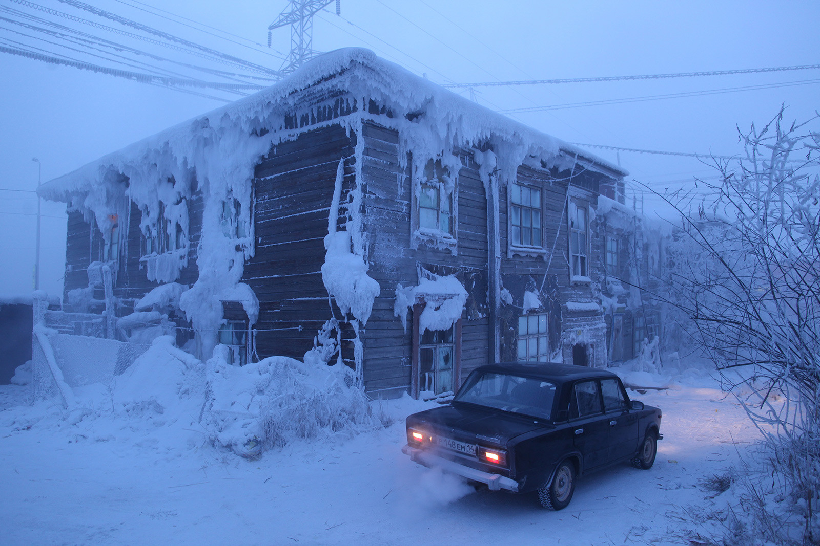 Руски автомобил със запален двигател пред заснежена сграда, покрита с лед, в най-студения град на света. Автомобилите в Якутск трябва да бъдат оставяни в топли гаражи или двигателят трябва да работи непрекъснато, в противен случай бензинът ще замръзне