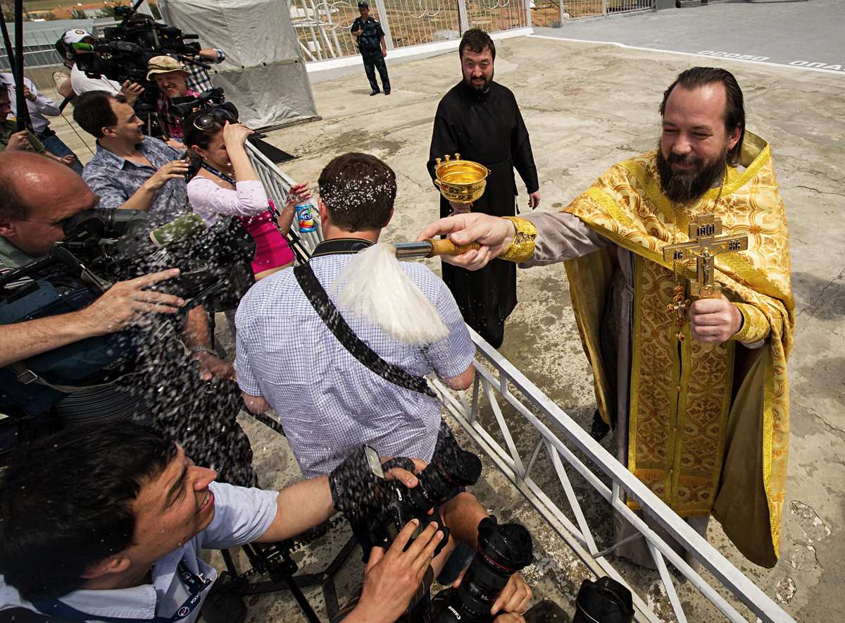 Православни свештени кропи светом водицом представнике медија на  космодрому Бајконур непосредно после освештавања ракете „Сојуз“.