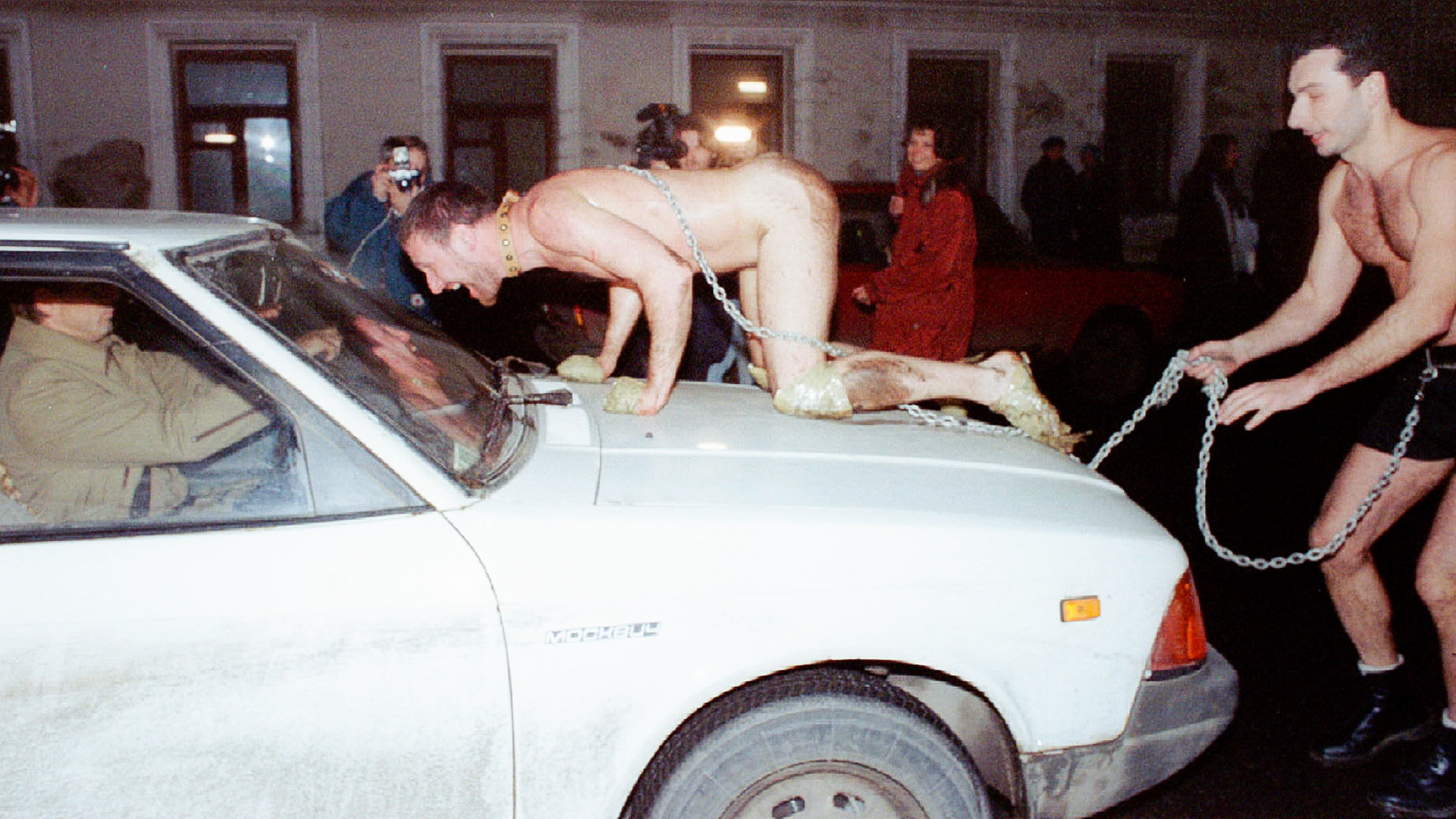 Russian artist Oleg Kulik imitating a dog jumps on the car of a scared Muscovite as Alexander Brener, representing his owner, tries to hold him back
