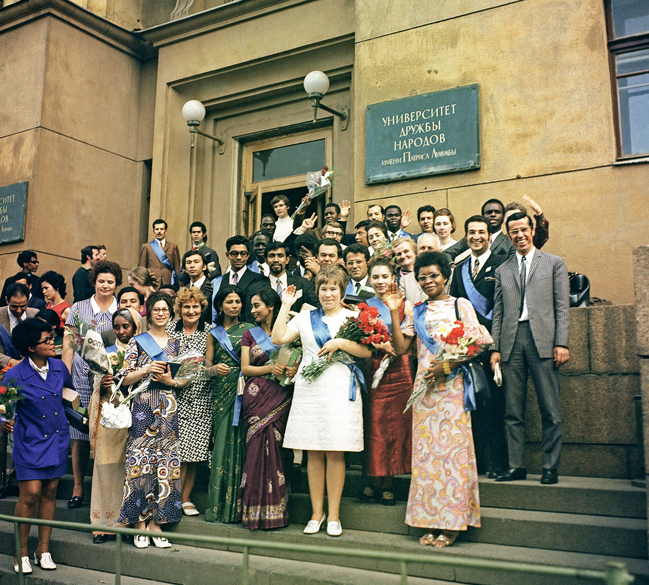 A group of UDN graduates posing for a picture in front of their alma mater.