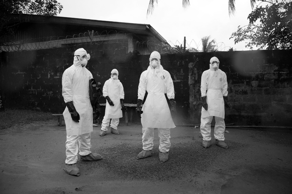 A body removal team waits for the house to be sprayed with chlorine before they enter to remove the body killed by Ebola.