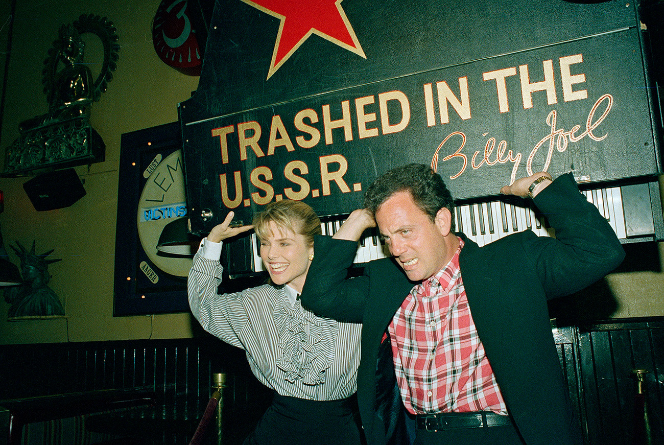 Rock star Billy Joel is helped by his wife Christie Brinkley, as he pretends to lift a piano suspended from the ceiling at the Hard Rock Cafe in New York,  June 3, 1988. Joel, donated the piano he used on his concert tour of the Soviet Union last year, to the cafe's collection of memorabilia. 
