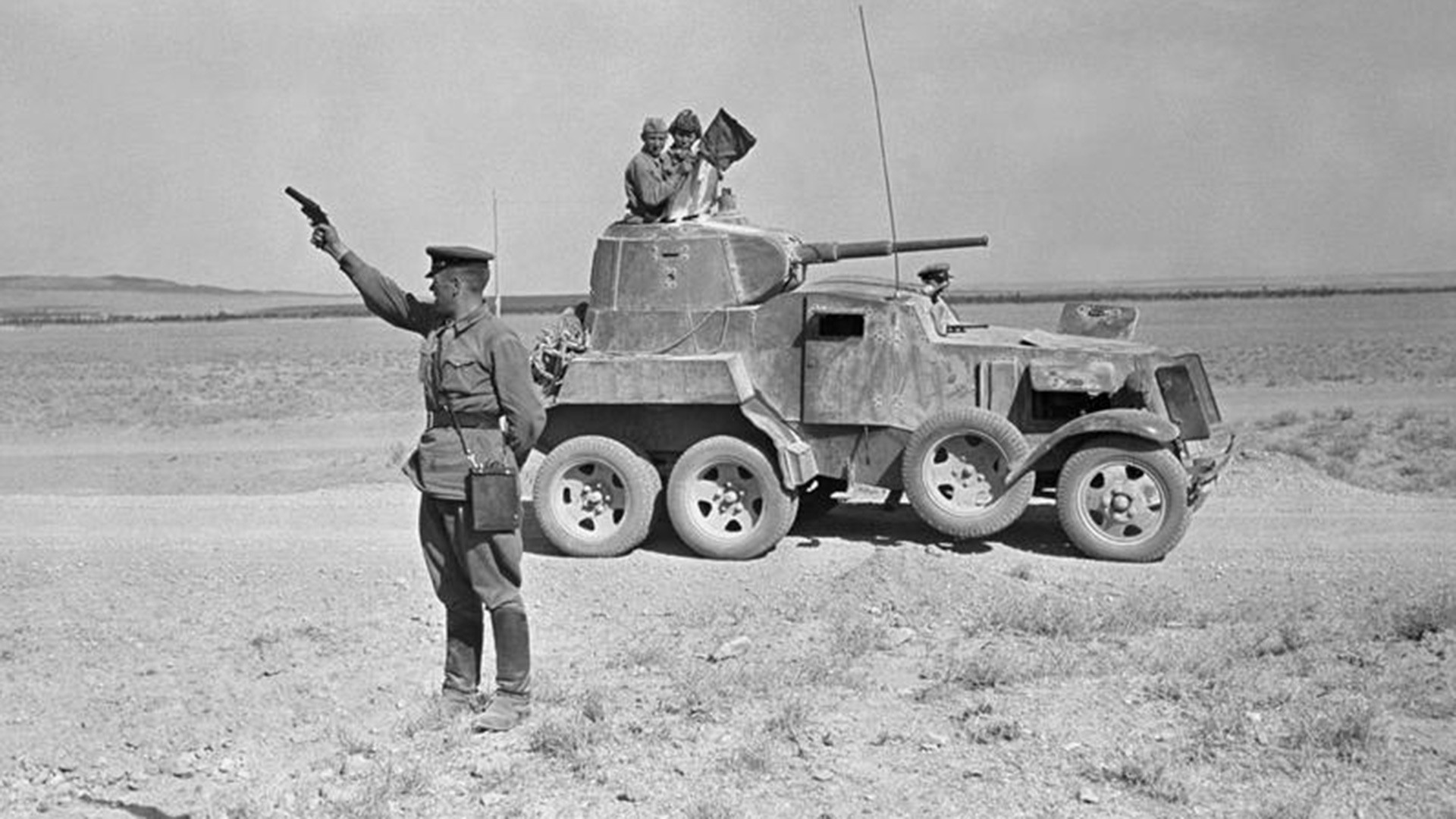 Sovjetski častnik drži v zrak signalno pištolo zraven oklepnega avtomobila BA-10 v iranski puščavi.