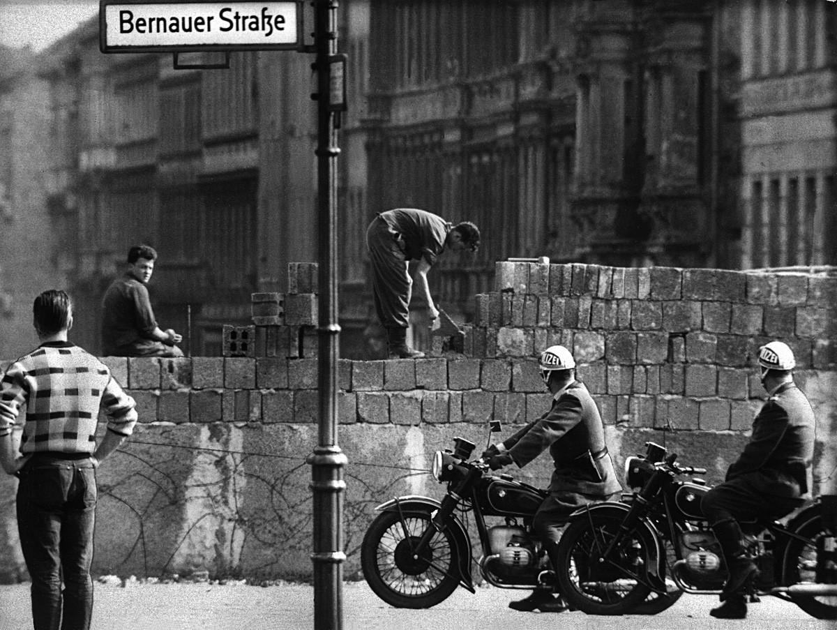 Dua polisi bermotor memperhatikan para pekerja meletakkan batu bata pada satu sisi Tembok Berlin di Bernauer Strasse, Berlin, Jerman, 13 Agustus 1961.