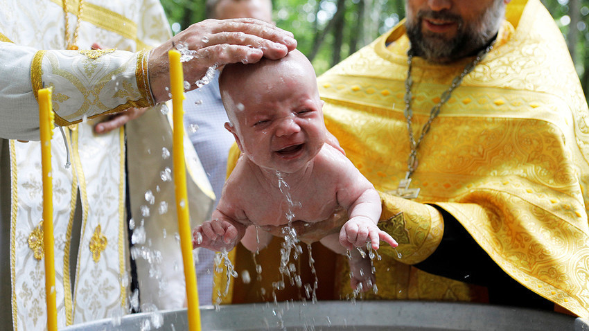 Padre ortodoxo batiza criança.