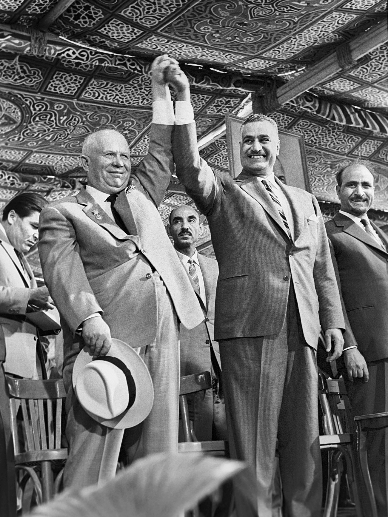 Le président de la République arabe unie Gamal Abdel Nasser et Nikita Khrouchtchev se tenant la main, et le président de la République arabe du Yémen Abdullah as-Sallal (à droite) lors d'une cérémonie dans le cadre d'une étape de la construction du réseau hydraulique d'Assouan
