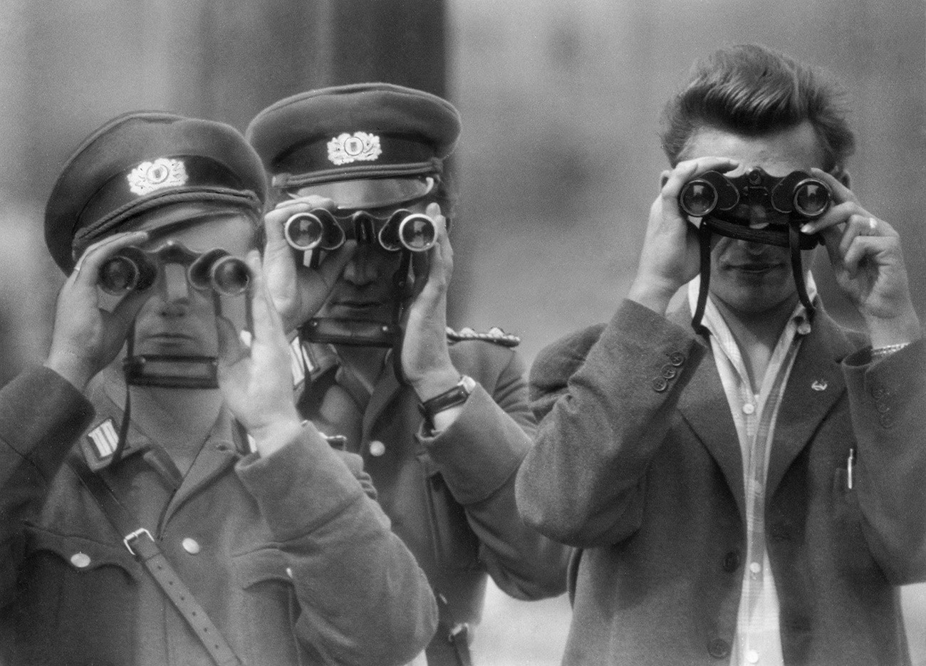 Deux policiers est-allemands et un civil observent avec des jumelles un photographe dans la région de Berlin-Ouest pendant la construction du mur de Berlin.