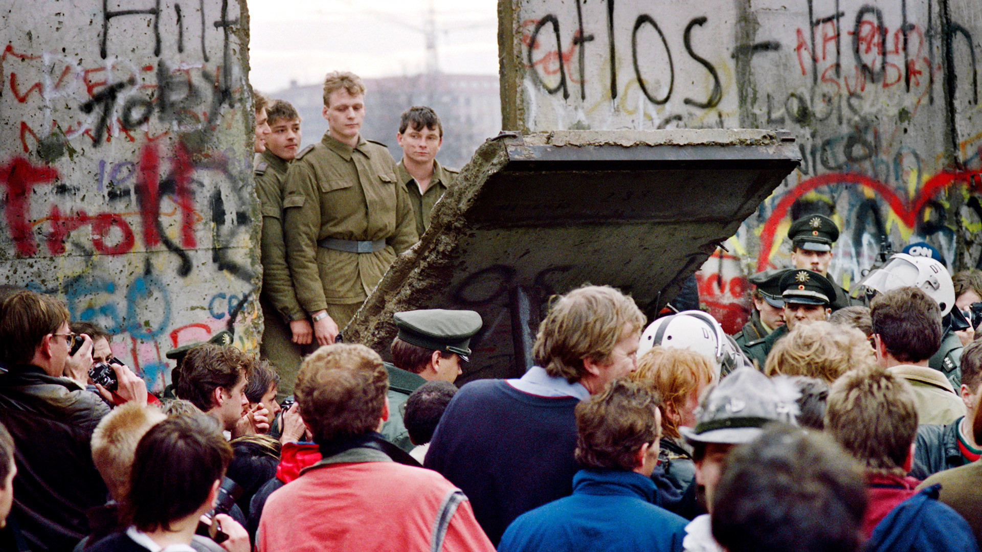Грађани Западног Берлина испред Берлинског зида 11. новембра 1989. посматрају како источнонемачки граничари руше део Берлинског зида како би направили нови гранични прелаз близу Постдамског трга. Два дана раније је Гинтер Шабовски изјавио да ће источни Немци од поноћи моћи слободно да напусте земљу.