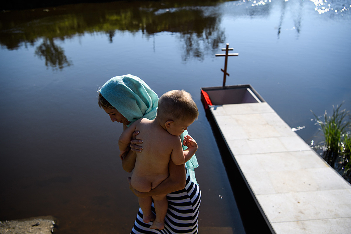 Seorang ibu dan anaknya di Sungai Chusovaya selama upacara pembaptisan massal Katedral Pangeran Vladimir di Desa Stantsionny-Polevskoi pada Hari Kristenisasi Rus.
