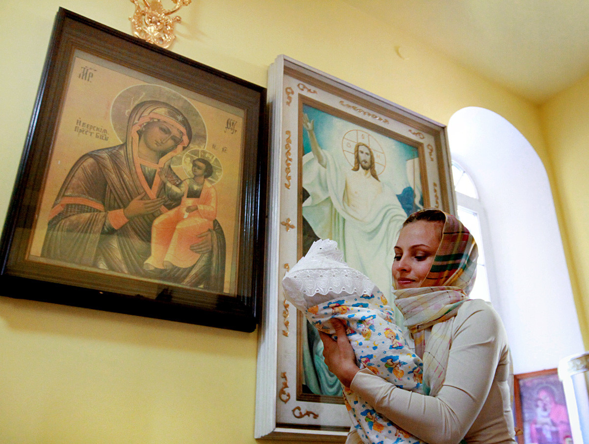 Seorang perempuan menggendong anaknya saat upacara pembaptisan bayi di Gereja Svyatitelya Nikolaya, Vladivostok.
