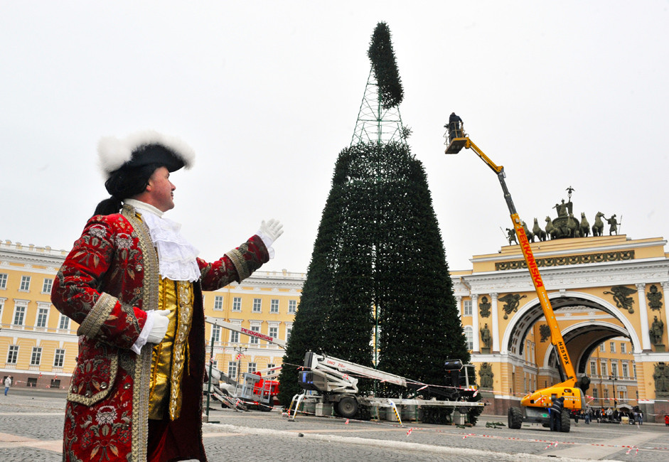 Guindastes são usados para montar a celebrada árvore de Natal da Praça do Palácio, em São Petersburgo, onde atores durante todo o ano se vestem de figuras históricas como Pedro, o Grande (esq.) para entreter os turistas.