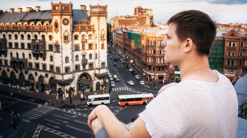 Seorang pemuda duduk di atap dan melihat ke Ploshchad Lva Tolstogo di Sankt Peterburg, Rusia.