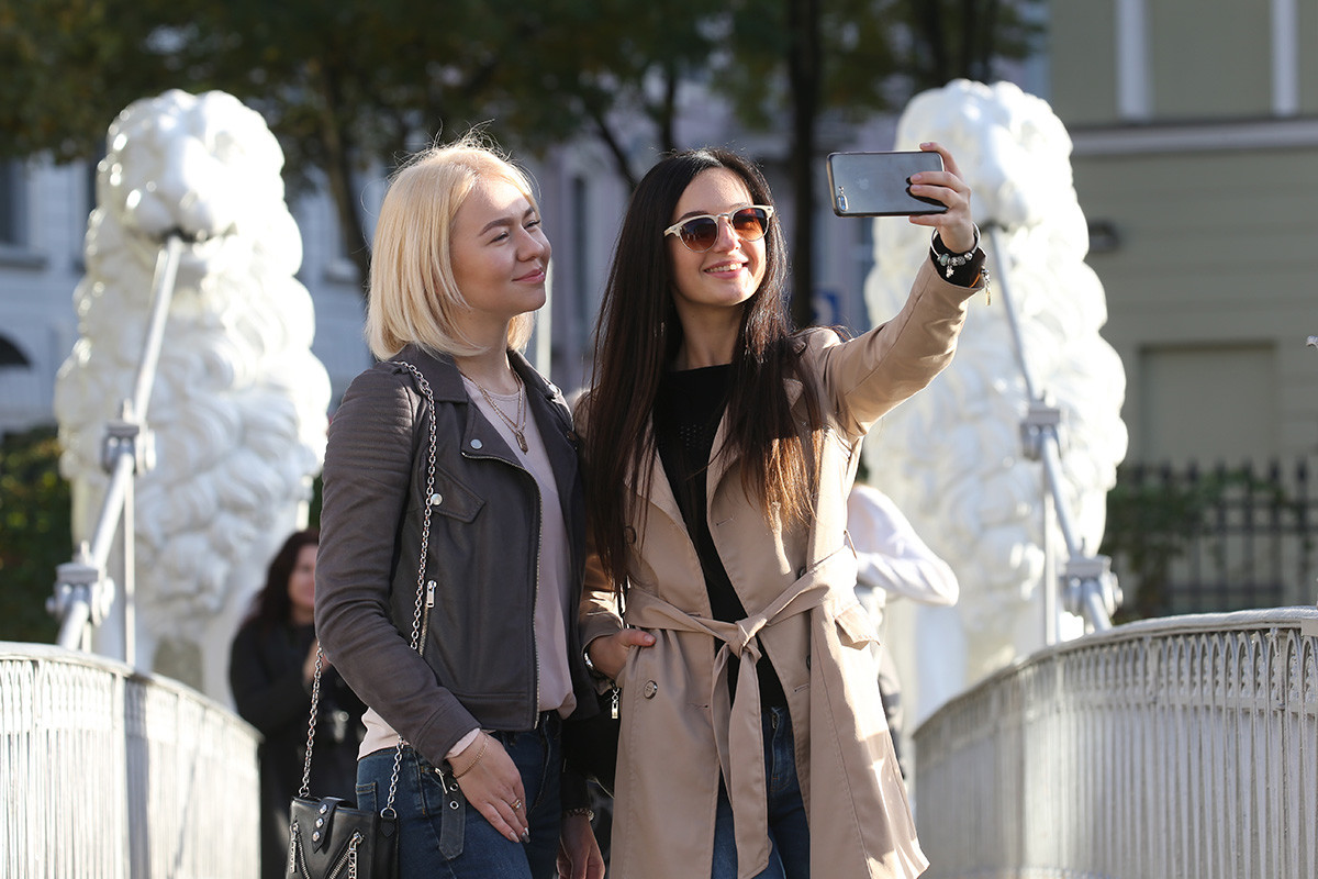 Young women take a selfie on the Lion Bridge (Bridge of Four Lions), a pedestrian bridge across the Griboyedov Canal in central St Petersburg