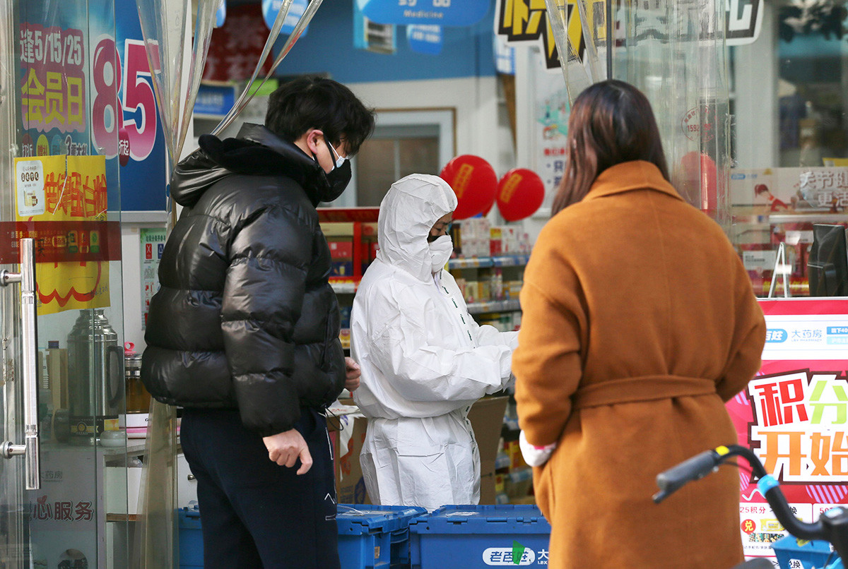A worker in protective suit serves customers at a pharmacy following an outbreak of the new coronavirus in Wuhan.