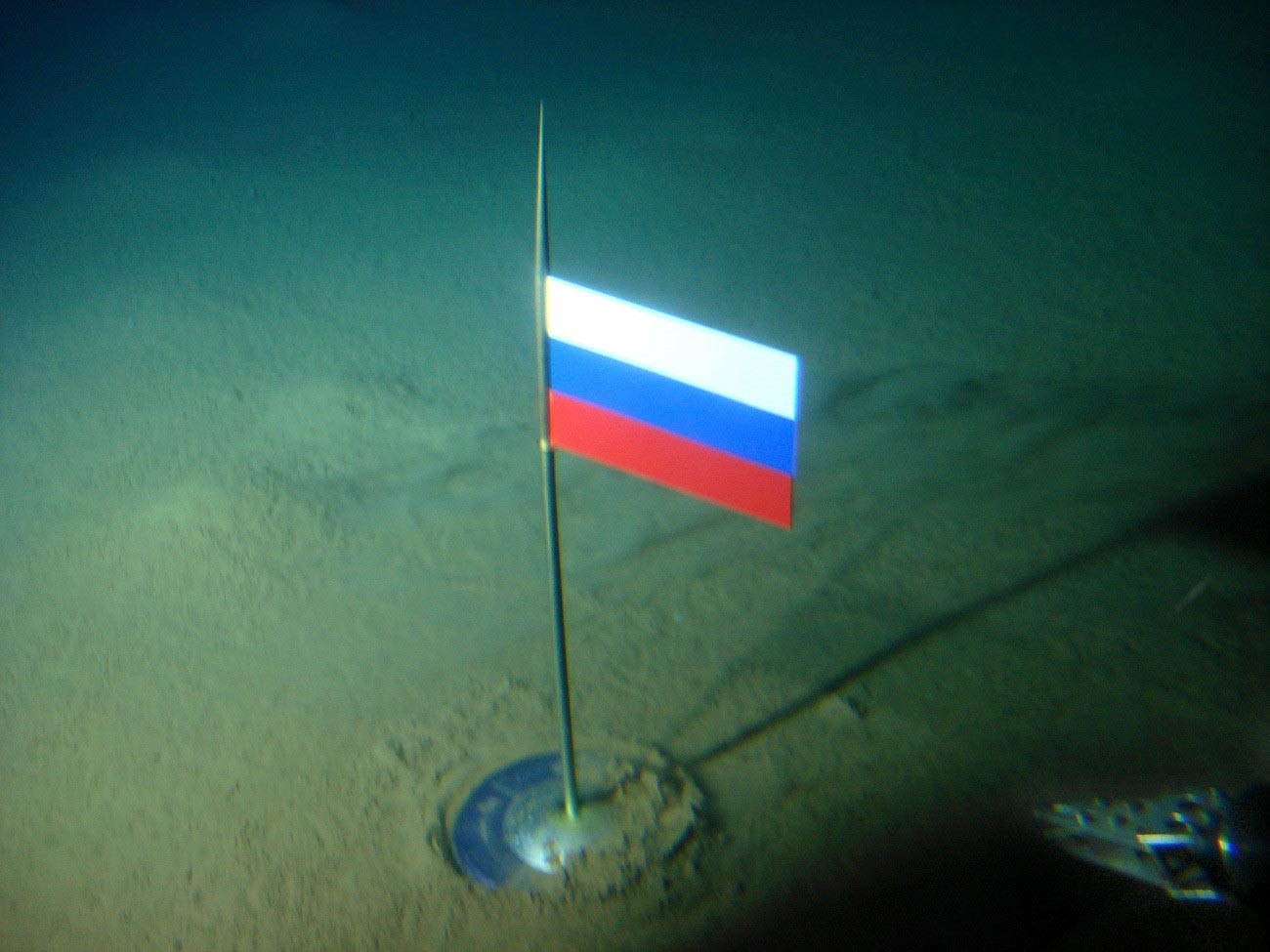Zastava Rusije s kapsulom od titanija na dnu oceana ispod Sjevernog pola, nekoliko sekundi nakon što je 2. kolovoza 2007. godine postavljena pomoću batiskafa Mir-1.
