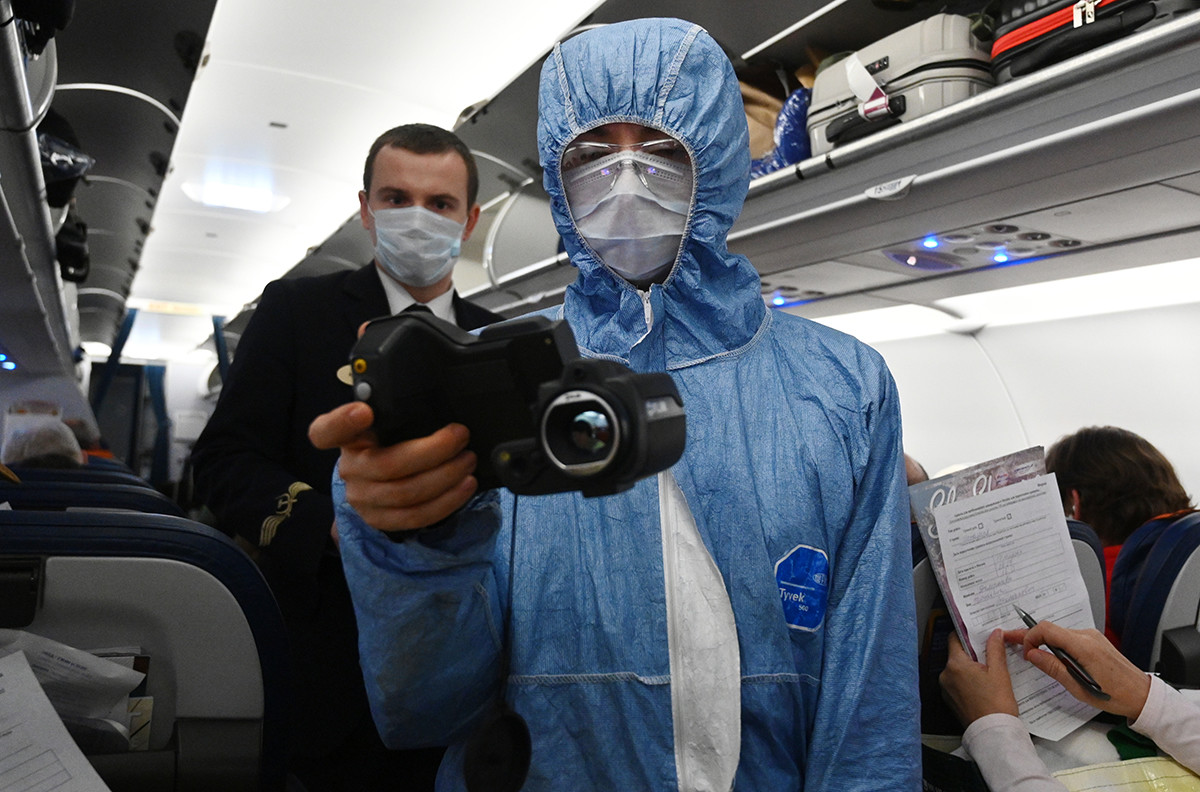 Сотрудник Роспотребнадзора проверяет тепловизором температуру у пассажиров на борту самолета в аэропорту Шереметьево в Москве.