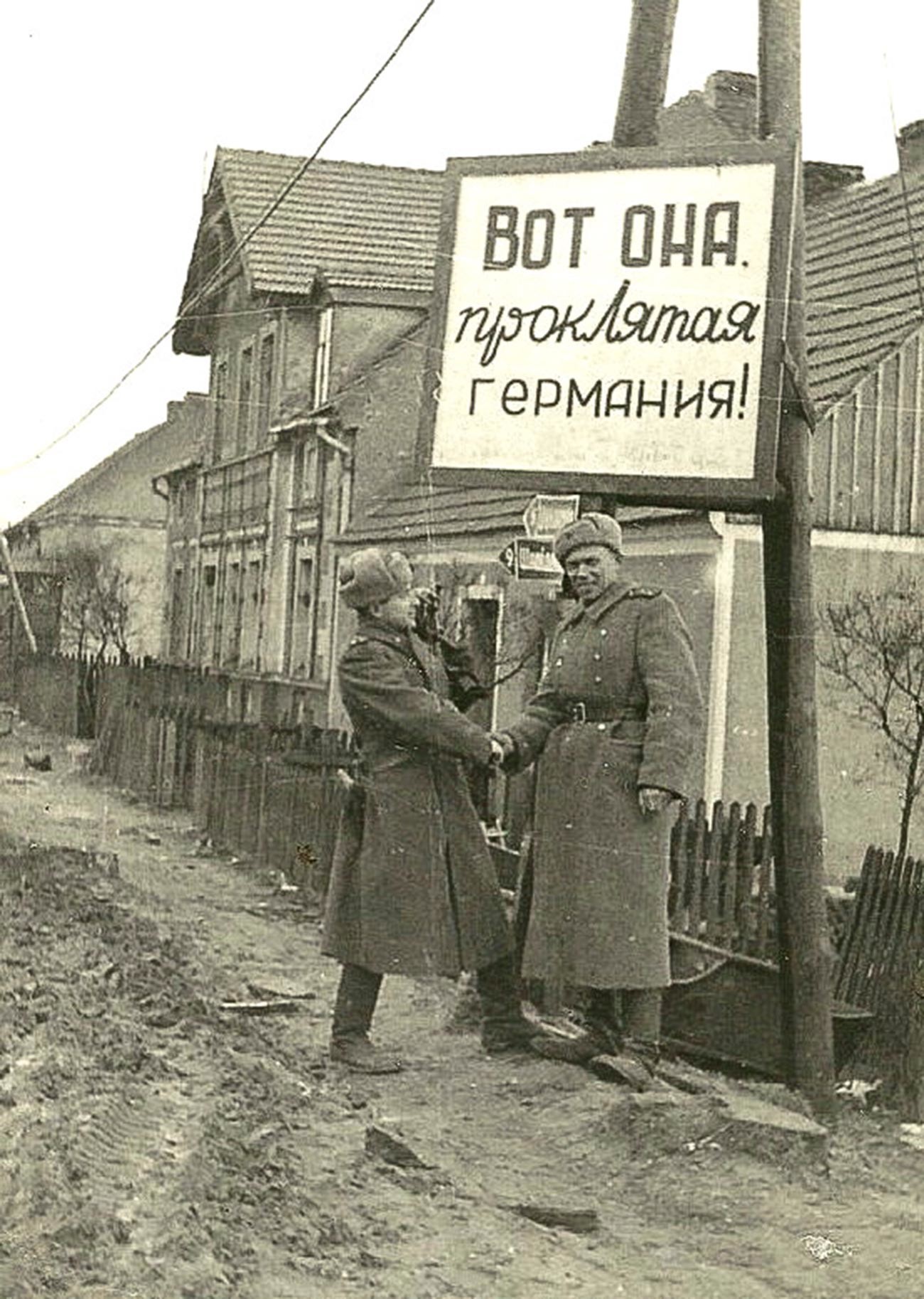 看板には「ここにいた、忌々しいドイツ！」の文言。『ポメラニアの戦い』を撮影中の戦場カメラマン、イリヤ・アロンス（左）とボリス・デメンチエフ。ポーランドとドイツの旧国境にて。1945年4月。