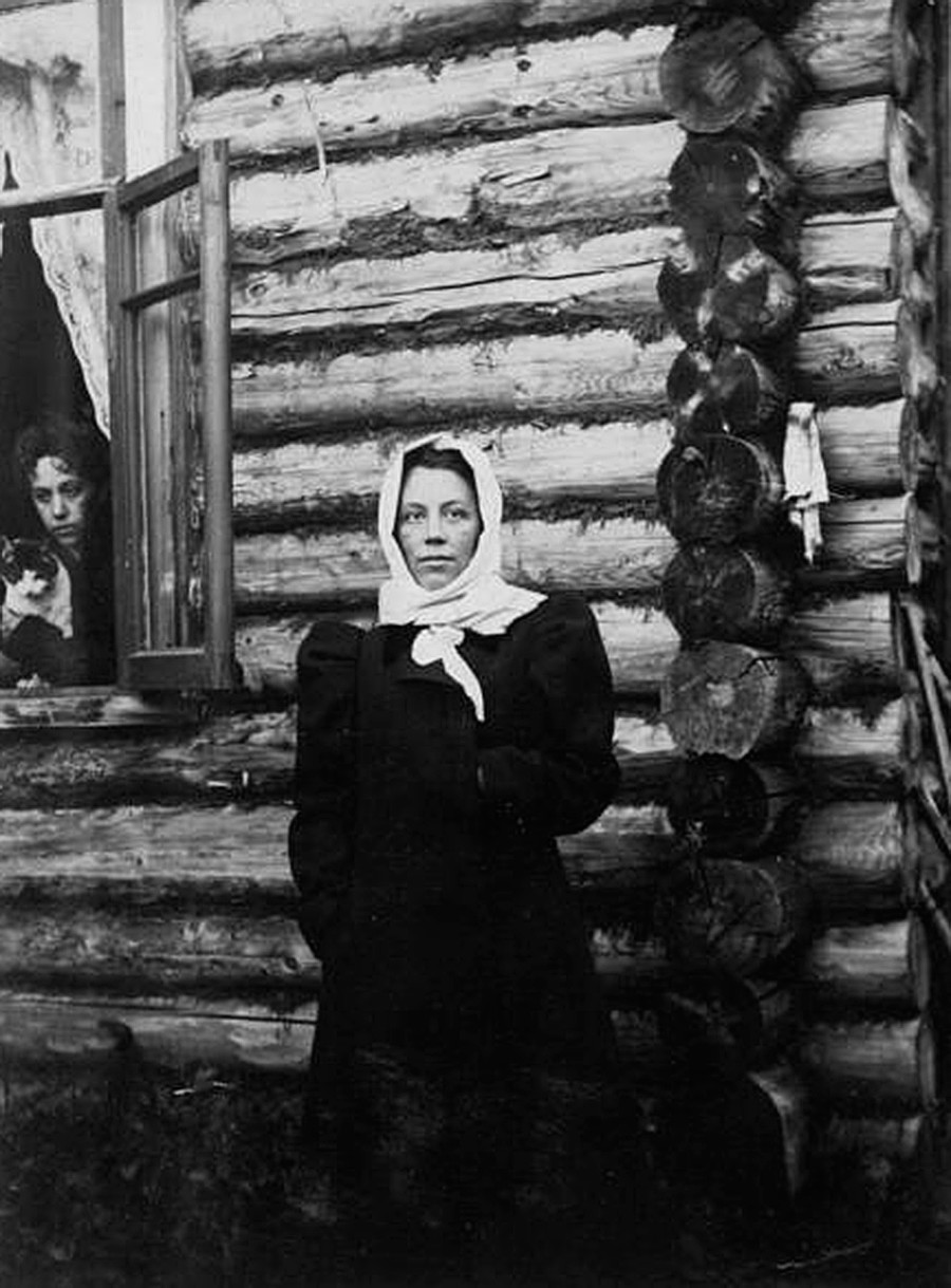 Seorang perempuan berdiri de depan rumah kayu.