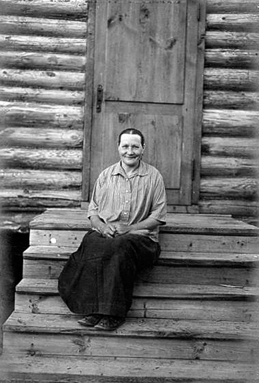 Retrato de mulher sentada à entrada de casa, em escada de madeira.