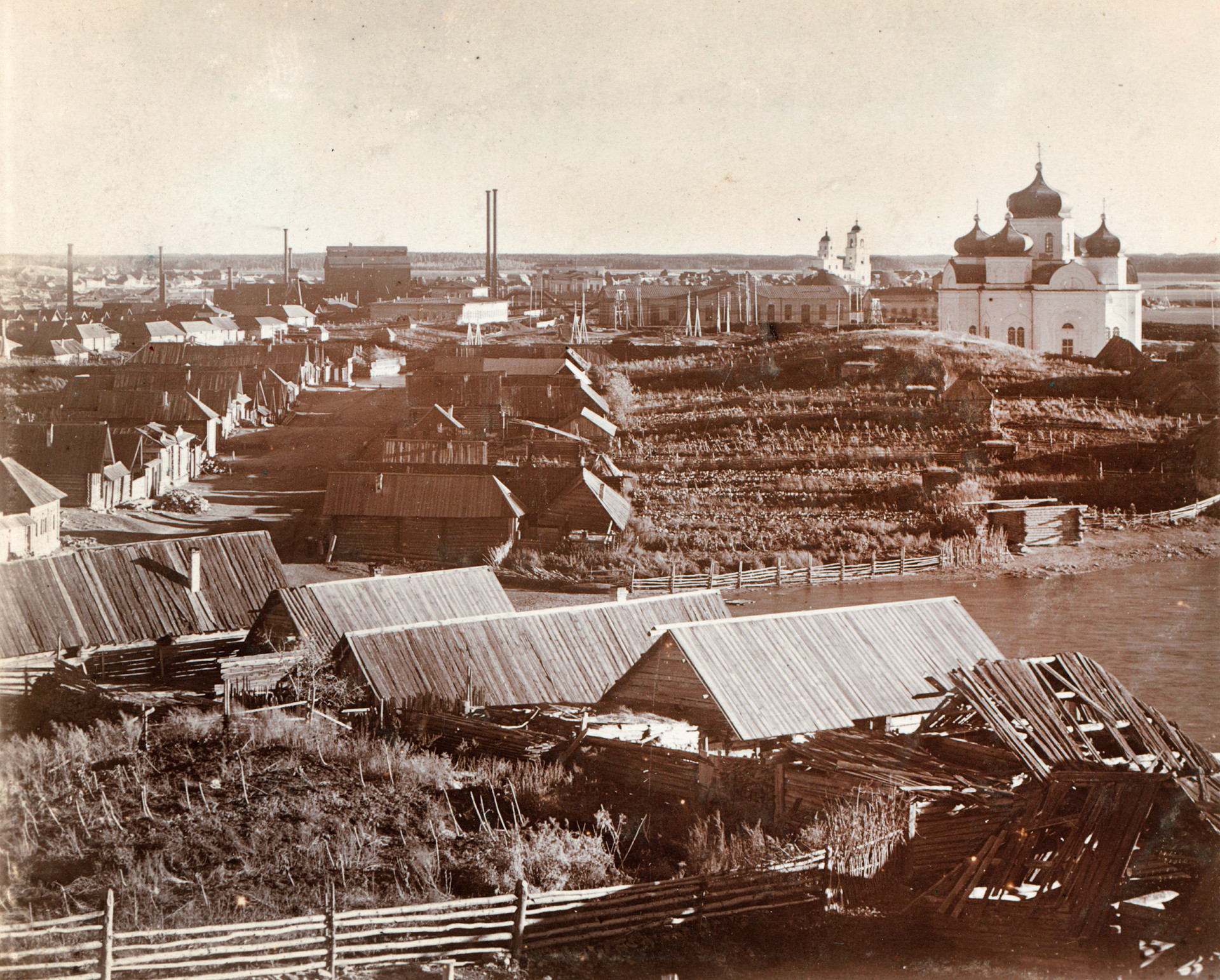 View of workers' houses & garden plots. Background: Kyshtym factory (left), Church of the Descent of the Holy Spirit, Cathedral of the Nativity of Christ. 1909.