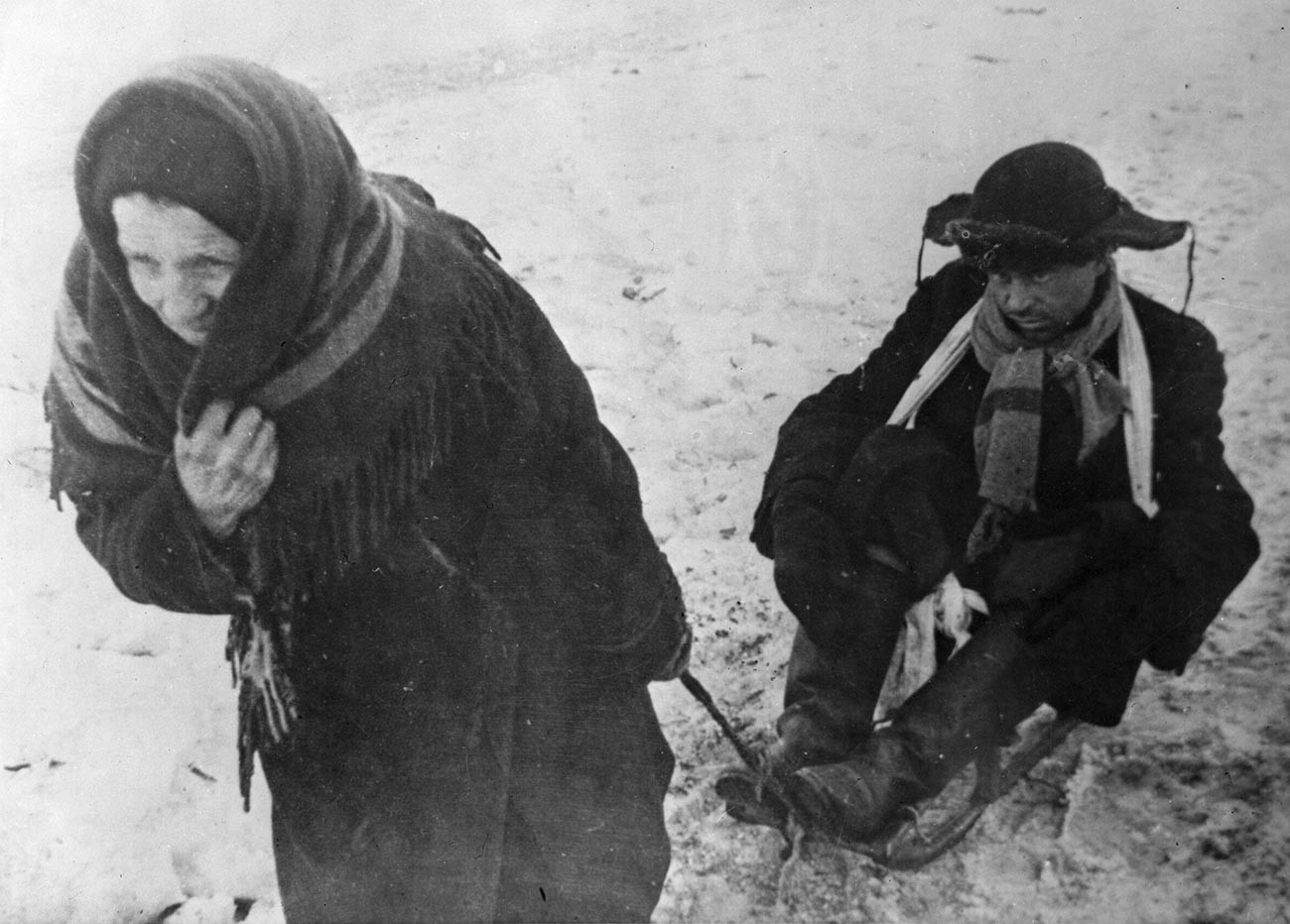 Ženska pelje na sankah moža, oslabelega zaradi lakote, v obleganem Leningradu med drugo svetovno vojno