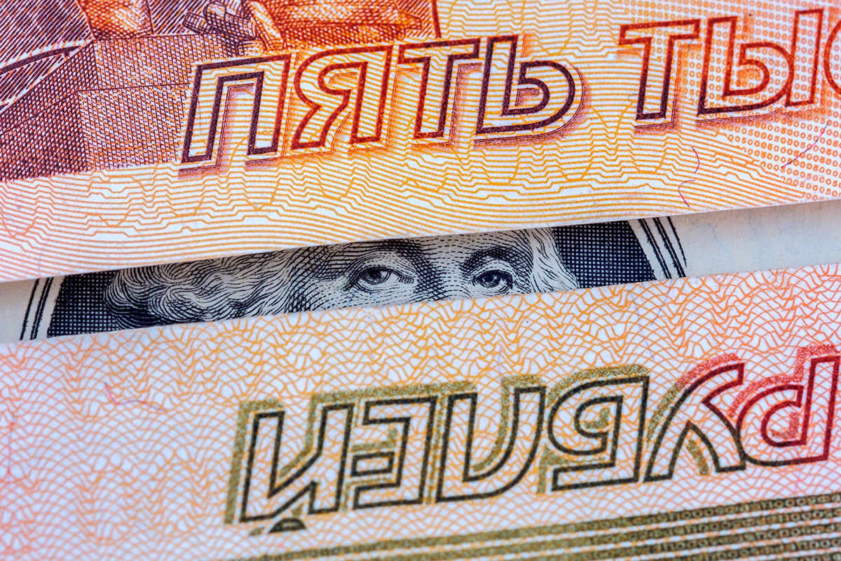George Wshington kuka z dolarskega bankovca med dvema bankovcema za pet tisoč rubljev.