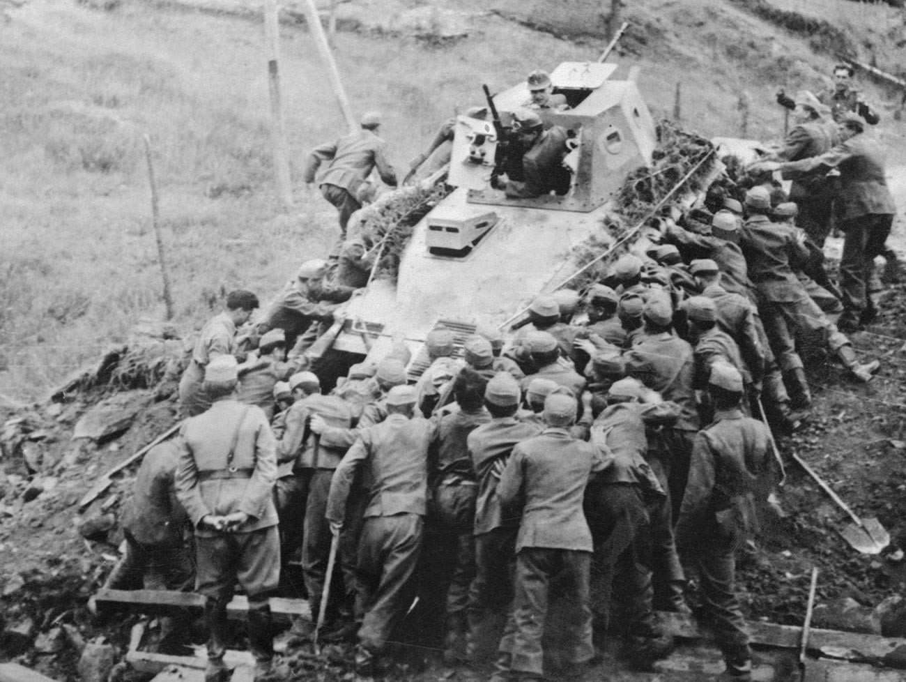 Más de 50 soldados húngaros están poniendo sus hombros a las ruedas en un esfuerzo por recuperar este tanque soviético inutilizado.