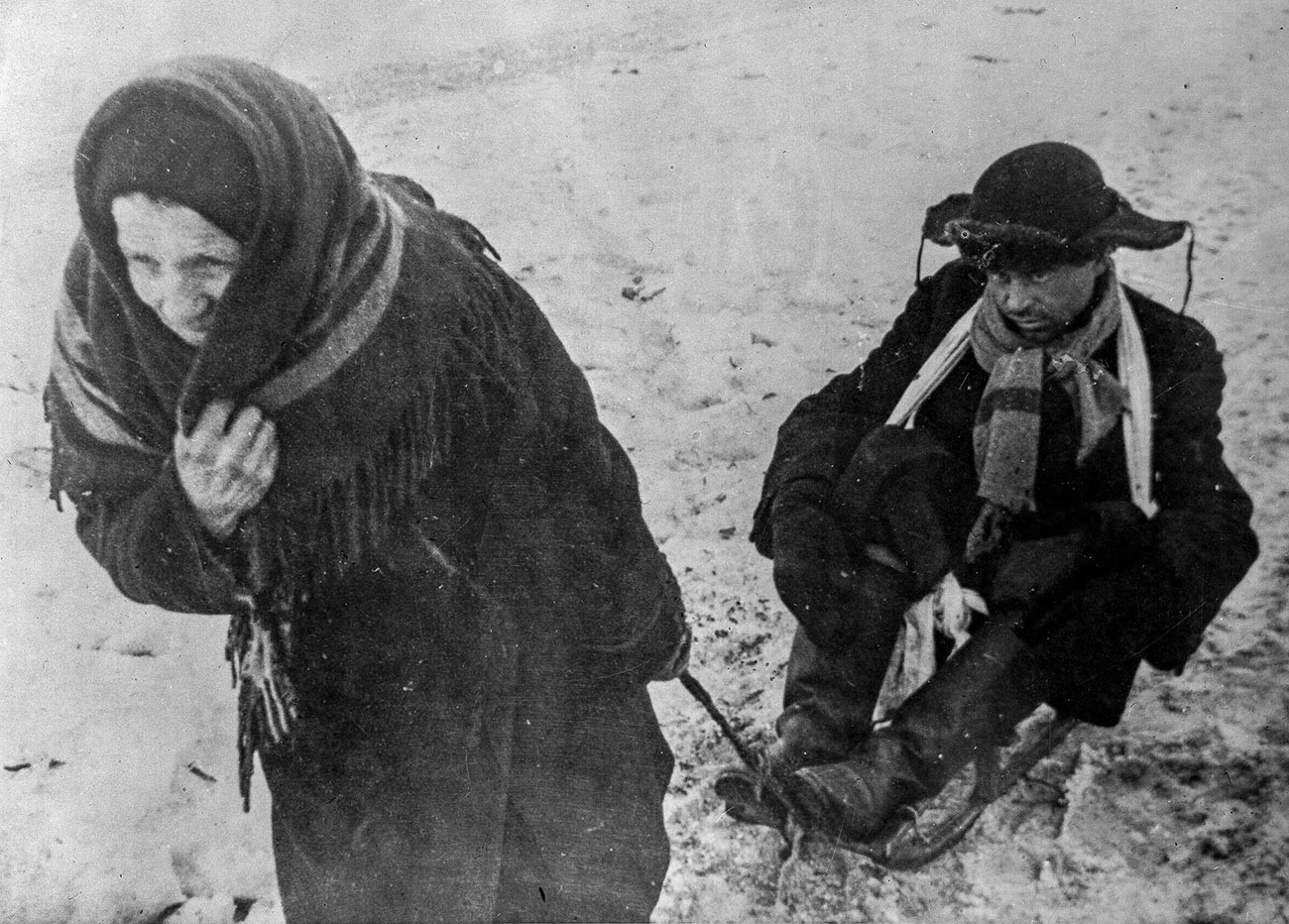 Блокадата на Ленинград (8 септември 1941 – 27 јануари 1944). Жена го влече на санка мажот кој е исцрпен од глад. Голема татковинска војна (1941-1945).
