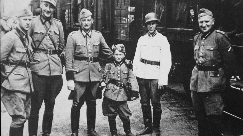 Алекс Курзем (трети оддесно) со пушка на рамото, во друштво на нацистички СС-офицери за време на Втората светска војна.
