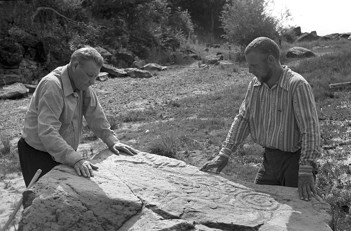 Академик Алексей Окладников и кандидат на историческите науки Александър Конопацки изследват петроглифите на скалата. Археологически разкопки в село Сикачи-Алян.