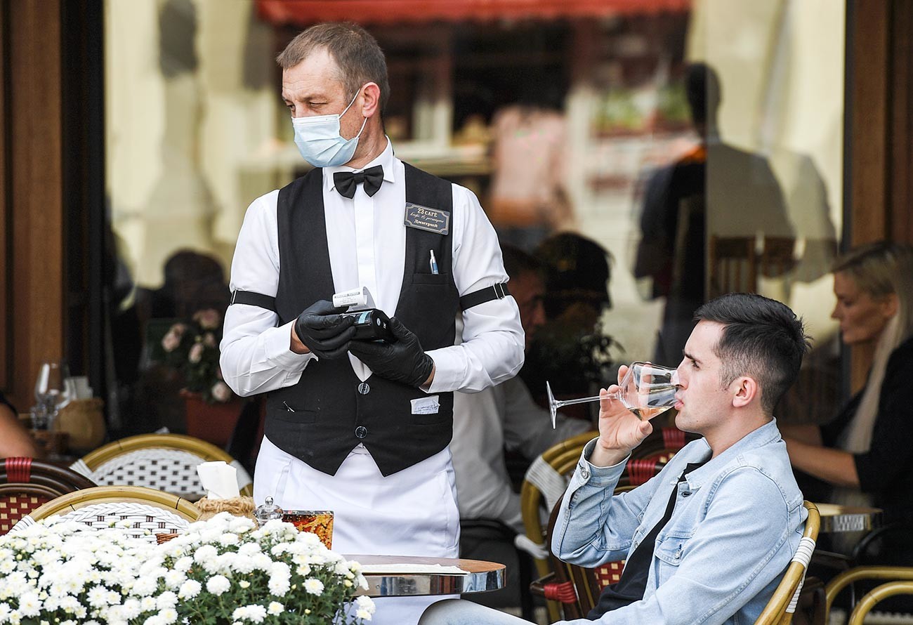 Официант в медицинской маске берет заказ у молодого человека в одном из кафе в Симферополе.
