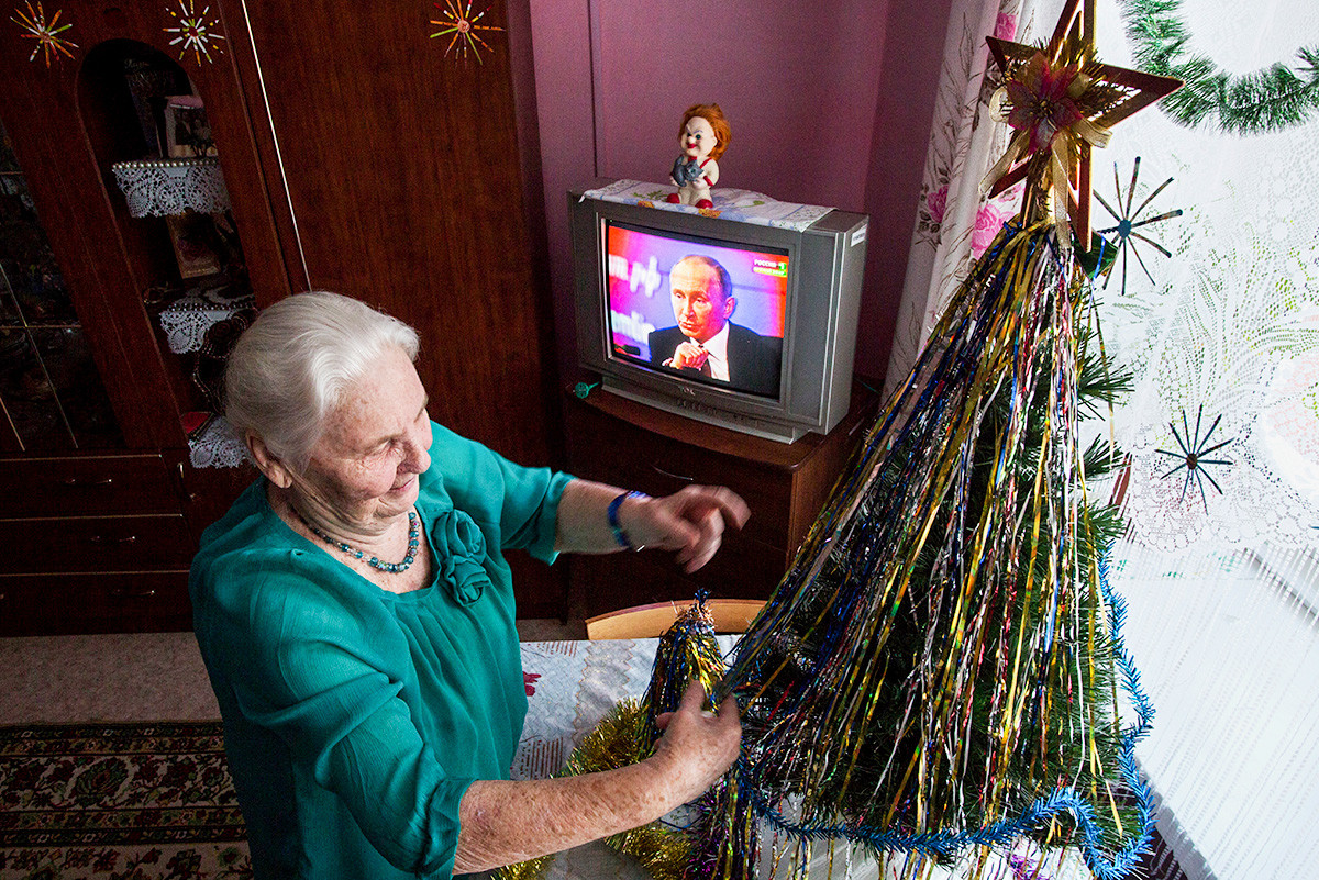 ОМСК, РУСИЯ - 23 ДЕКЕМВРИ 2016: Възрастна жена украсява коледно дърво, докато гледа на живо речта на Владимир Путин в дома за стари хора в Нежински.