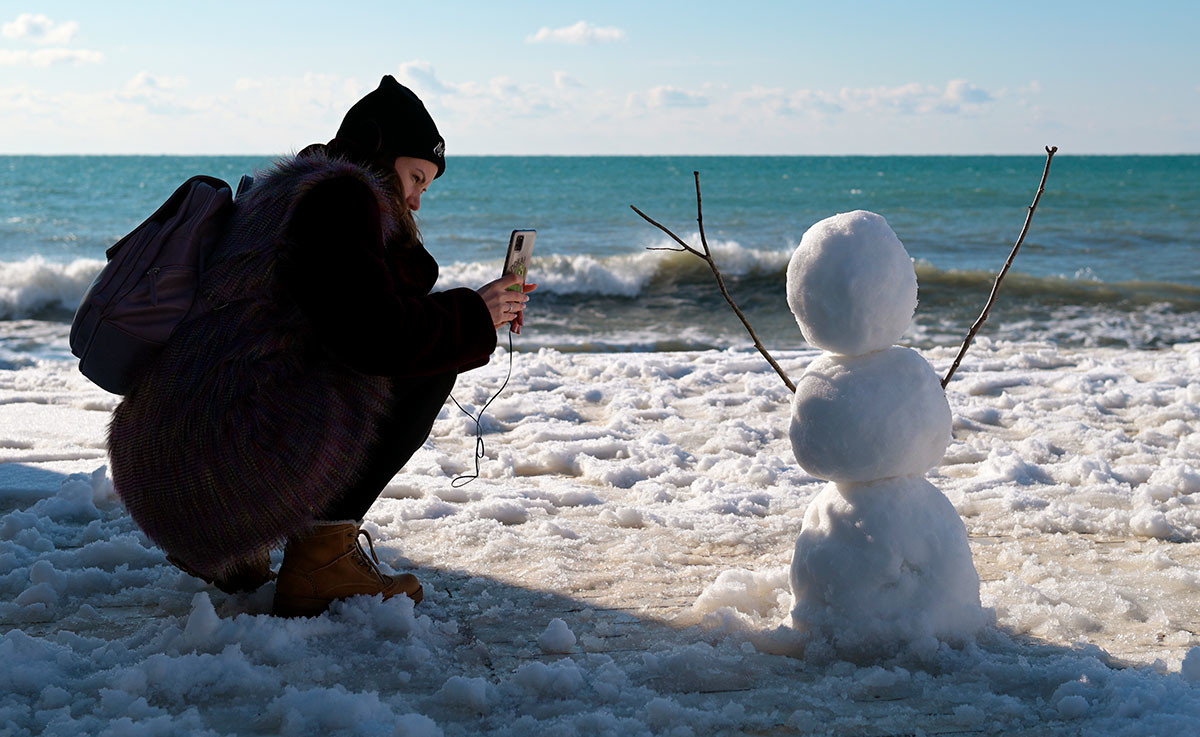Dekle fotografira snežaka na plaži v Adlerskem okraju, južno od Sočija.