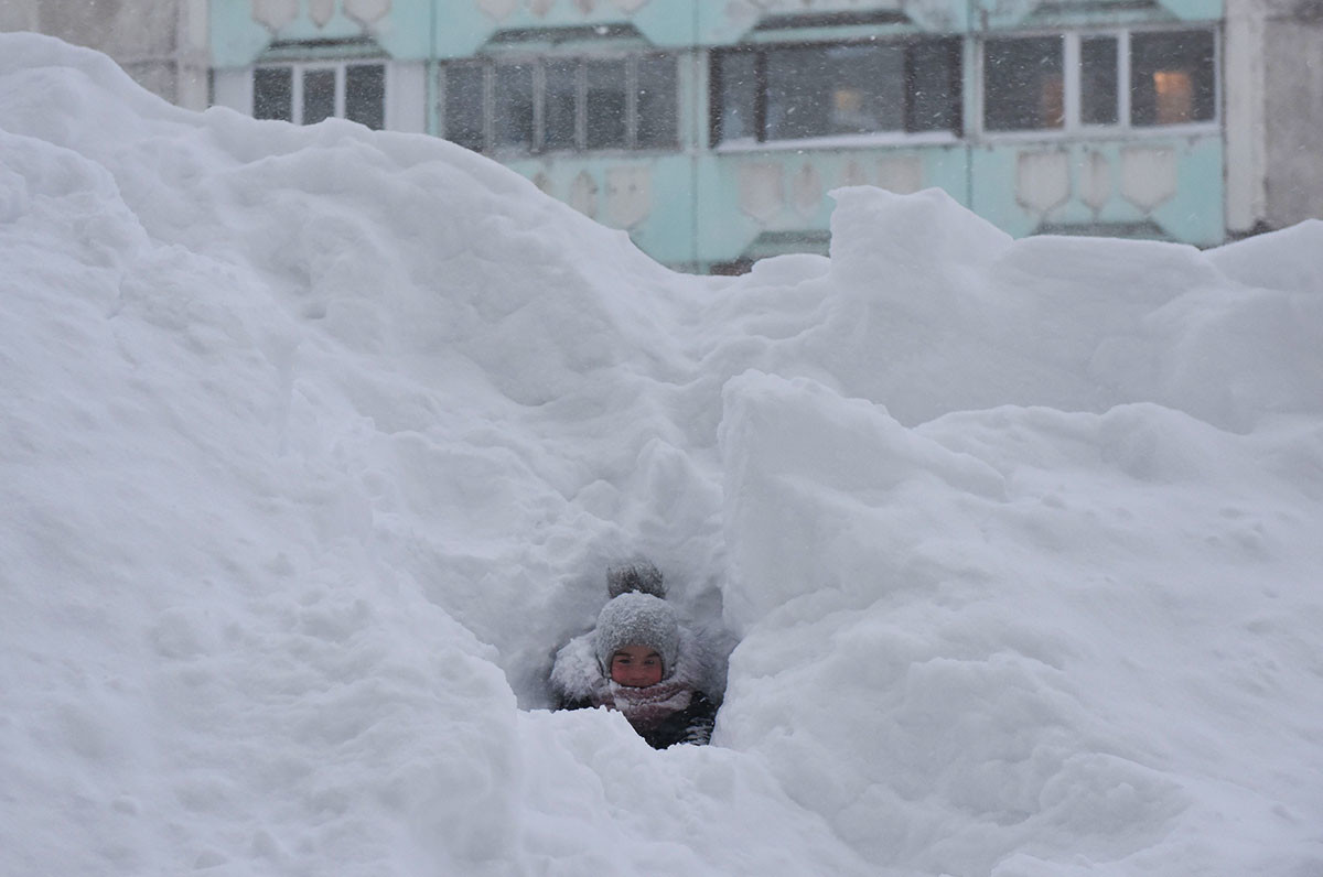 Дете играе в снежна преспа в двора на жилищна сграда в Норилск.