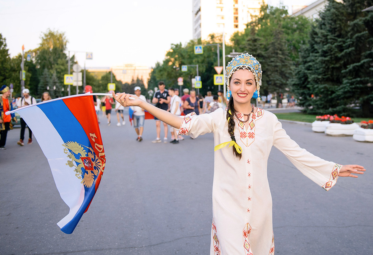 SAMARA, RUSIJA - 25. JUNIJ 2018: Ruska nogometna navijačica v tradicionalni ruski obleki z državno zastavo pred nogometno tekmo svetovnega pokala FIFA 2018 med Rusijo in Urugvajem. 