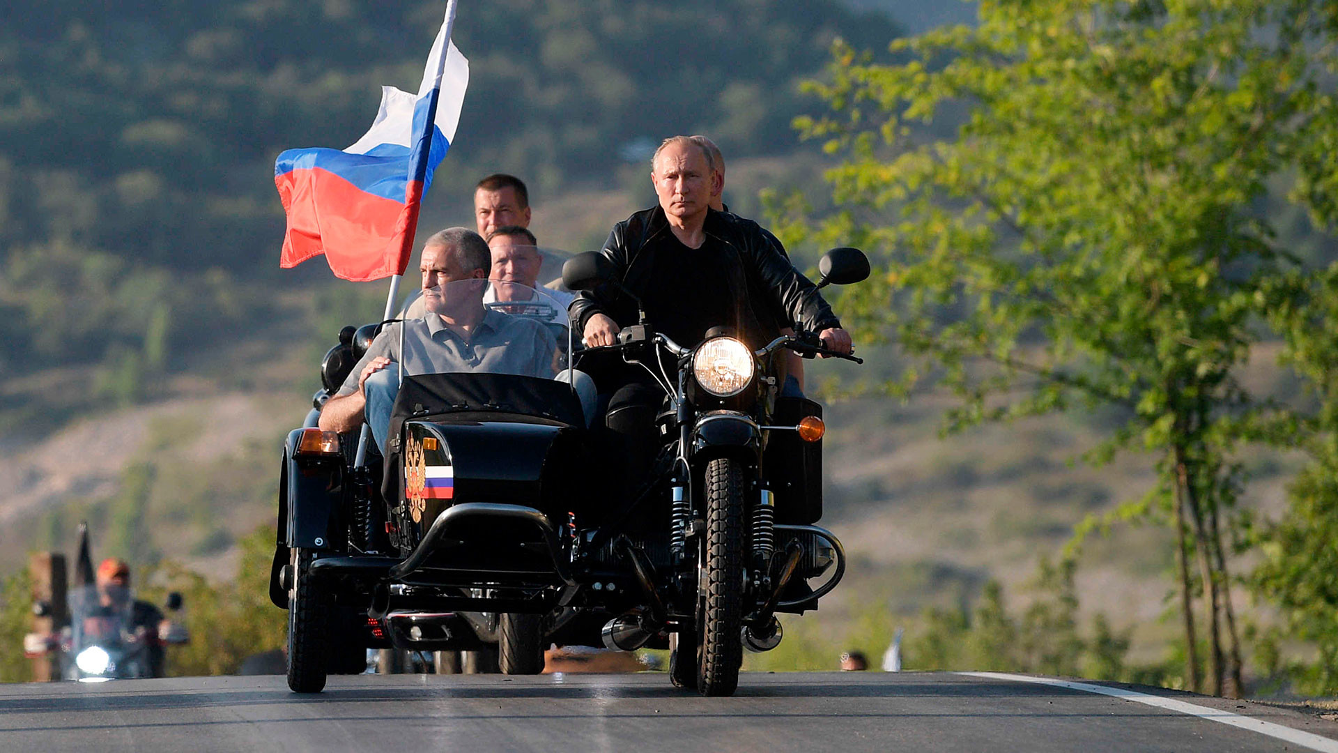 Presiden Rusia Vladimir Putin mengendarai sepeda motor Ural dengan sespan selama pameran sepeda motor internasional di Sevastopol, Krimea, 10 Agustus 2019. Putin berkendara bersama Kepala Republik Krimea Sergey Aksenov (kiri).