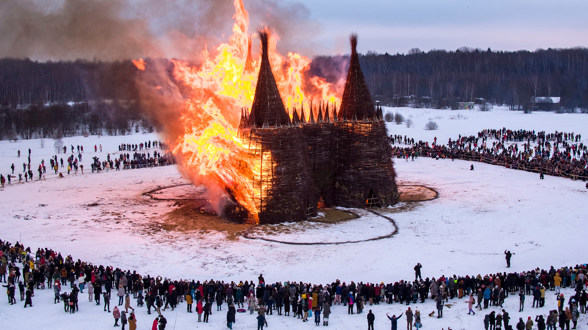 People watch a castle-shape wooden construction burning as part of celebrations at the Maslenitsa (Shrovetide) festival at the Nikola-Lenivets art park in Nikola-Lenivets village, about 200 kilometers (125 miles) south-west of Moscow, Russia, Saturday, March 13, 2021