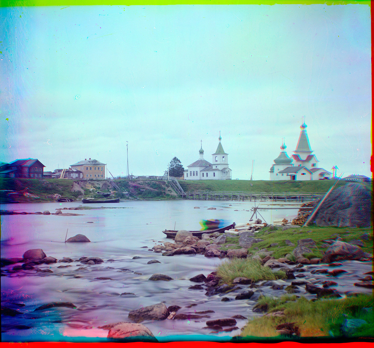 Shuyeretskoye. View across Shuya River with wooden Church of St. Clement (center), Church of St. Paraskeva & St. Nicholas Church. Smudge in the skiff is a person moving during the three exposures of the color process. Summer 1916