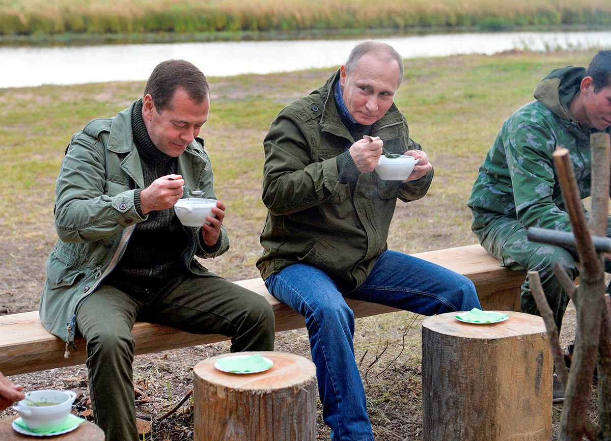 Presiden Rusia Vladimir Putin (tengah) dan Perdana Menteri Dmitry Medvedev (kiri) menyantap makanan setelah berkeliling Danau Ilmen di Novgorod, Rusia, 10 September 2016.